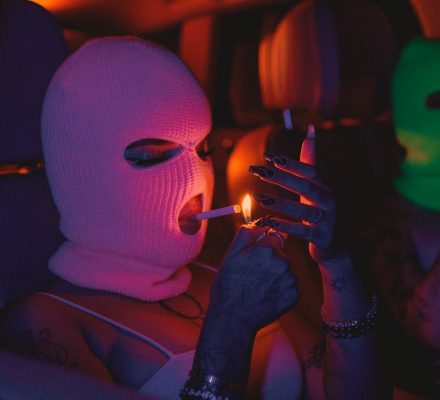woman in mask lighting cigarette while sitting in car